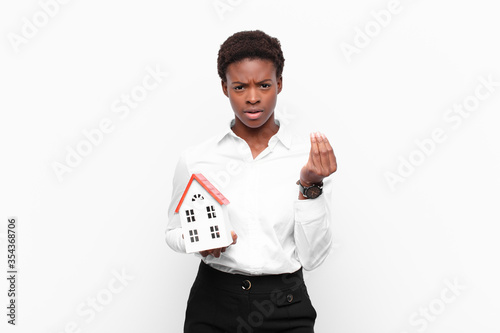 young pretty black womanmaking capice or money gesture, telling you to pay your debts! with a house model photo