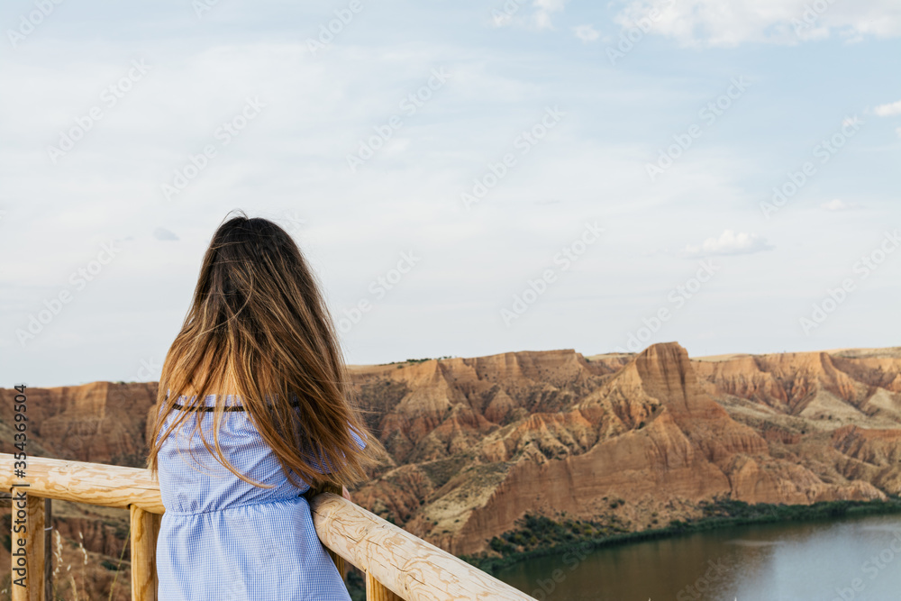 Girl in blue dress looking at the water canyon. Dry rocky landscape. Water canyon and rock erosion.