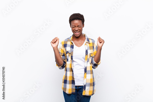 young pretty black womanlooking extremely happy and surprised, celebrating success, shouting and jumping photo