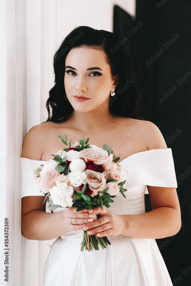 Bride brunette girl of European appearance. Large single portrait with a bouquet of flowers. Wedding makeup and hairstyle. Model. Morning of the bride or fees. Puffy lips and expressive eyes Bride brunette girl of European appearance. Large single portrait with a bouquet of flowers. Wedding makeup and hairstyle. Model. Morning of the bride or fees. Puffy lips and expressive eyes