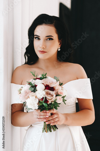 Bride brunette girl of European appearance. Large single portrait with a bouquet of flowers. Wedding makeup and hairstyle. Model. Morning of the bride or fees. Puffy lips and expressive eyes
