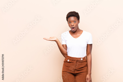 young pretty black womanlooking surprised and shocked, with jaw dropped holding an object with an open hand on the side photo