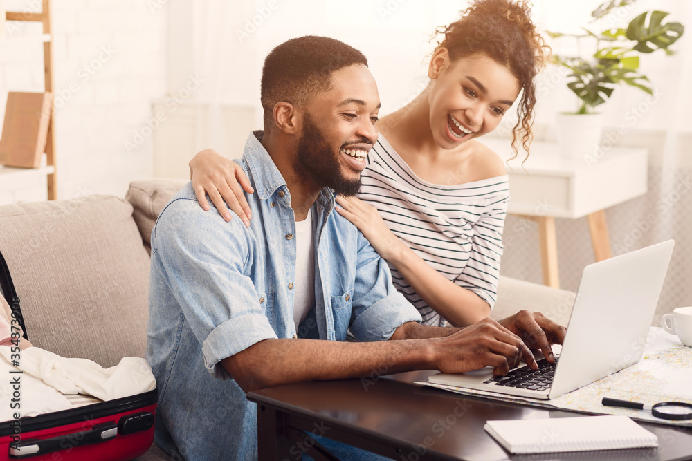 Joyful African American Couple Using Laptop Sitting At Table Indoors. Joyful African American Couple Using Laptop Sitting At Table Indoors.
