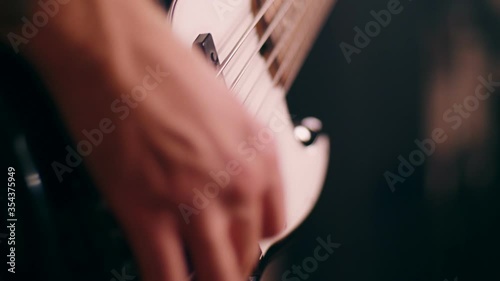 Close-up male hands of tattooed bassist guy playing on electric bass guitar at rock performance