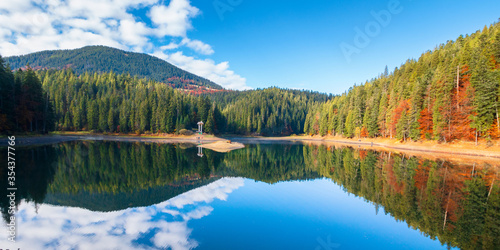 synevyr lake at foggy sunrise. misty mountain landscape in autumn. forest reflecting in the water. morning in fall season. trees in colorful foliage