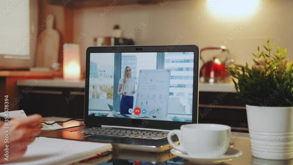 Online video conference on laptop with business woman speaker in home office. In the foreground: writing hands and a cup. Online video conference on laptop with business woman speaker in home office. In the foreground: writing hands and a cup.