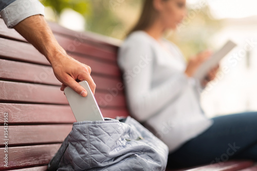 Pickpocket Thief Stealing Mobile Phone From Woman's Bag In Park photo