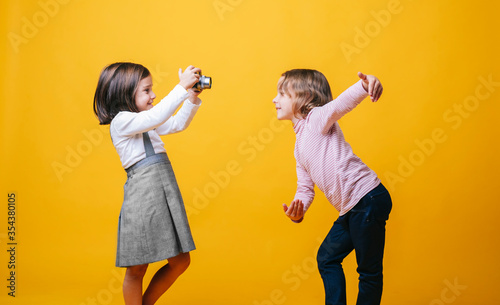 Two girls with a photo camera on yellow background. High quality photoA girl takes photos of another girl with a photo camera on a yellow background photo