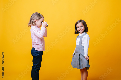 Two girls with a photo camera on yellow background. High quality photoA girl takes photos of another girl with a photo camera on a yellow background photo
