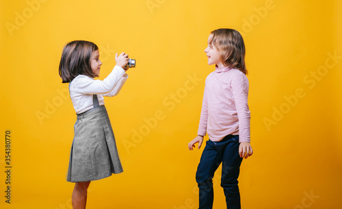 Two girls with a photo camera on yellow background. High quality photoA girl takes photos of another girl with a photo camera on a yellow background photo