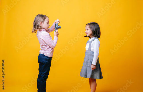Two girls with a photo camera on yellow background. High quality photoA girl takes photos of another girl with a photo camera on a yellow background photo