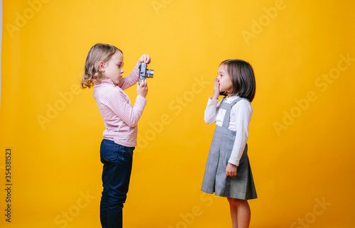 Two girls with a photo camera on yellow background. High quality photoA girl takes photos of another girl with a photo camera on a yellow background photo