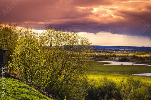 Bright landscape with young green foliage of trees backlit by the sun against a dramatic sunset