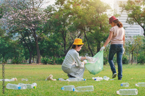 Two girl friends picking a used plastic bottle  in the garbage bags, The used plastic bottles were dumped into the lawn, take care environment concept