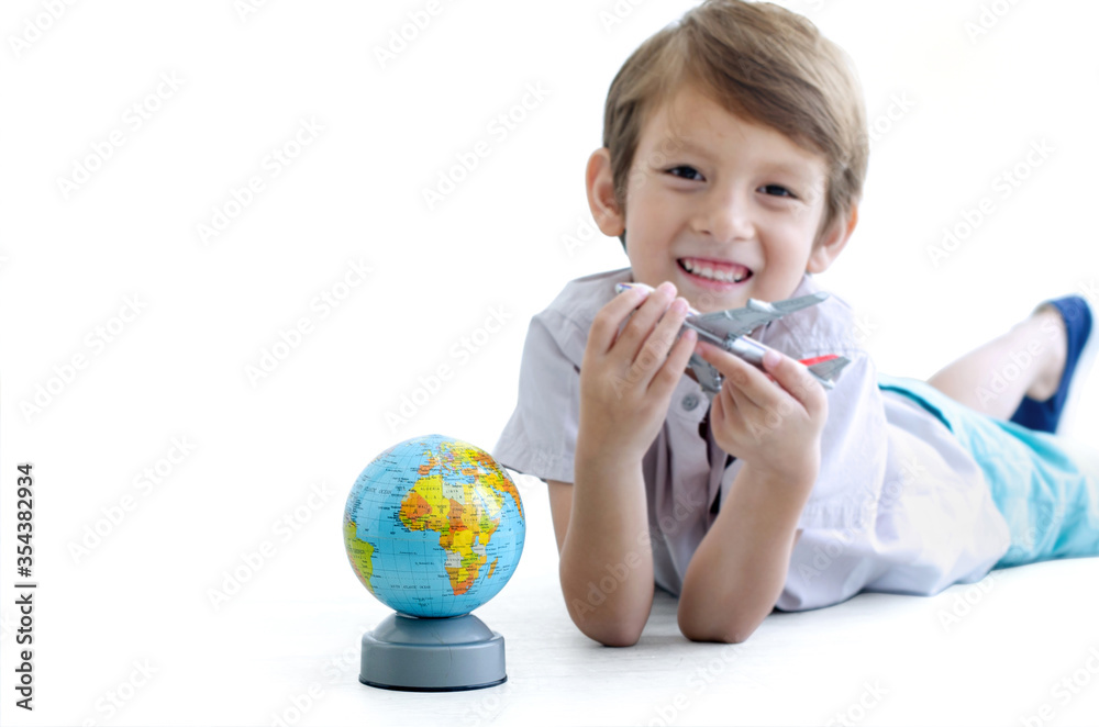 Little smiling boy is lying down on a floor playing airplane and globe on white background, selective focus, with clipping path Little smiling boy is lying down on a floor playing airplane and globe on white background, selective focus, with clipping path