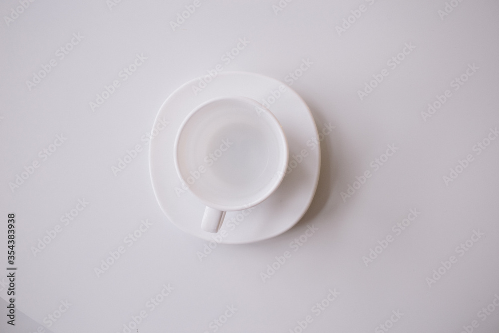 A white cup for tea or coffee on the white plate on the white table or background. flat lay. still life A white cup for tea or coffee on the white plate on the white table or background. flat lay. still life