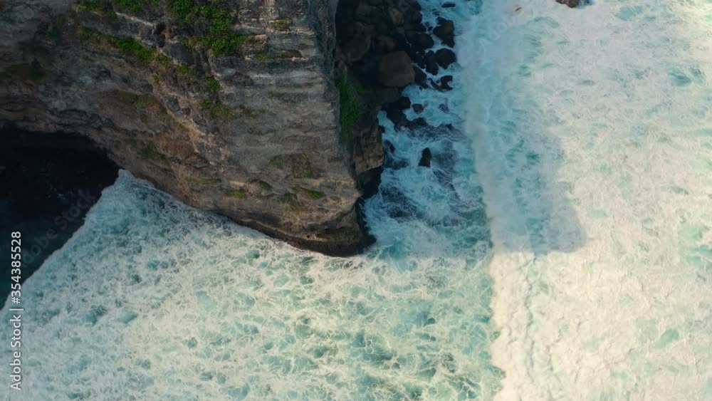 Aerial view of ocean waves beat into cracks in the rocks and a powerful jet of water breaks out of them. Danger water blow. Sea waves and water crashing on a rocky beach aerial view drone shot. Aerial view of ocean waves beat into cracks in the rocks and a powerful jet of water breaks out of them. Danger water blow. Sea waves and water crashing on a rocky beach aerial view drone shot.