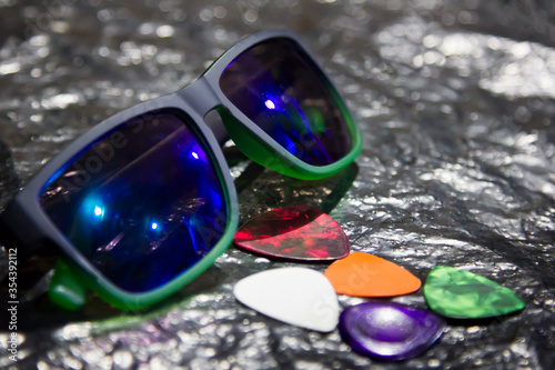 A composition of glasses and guitar picks lying on a metal surface