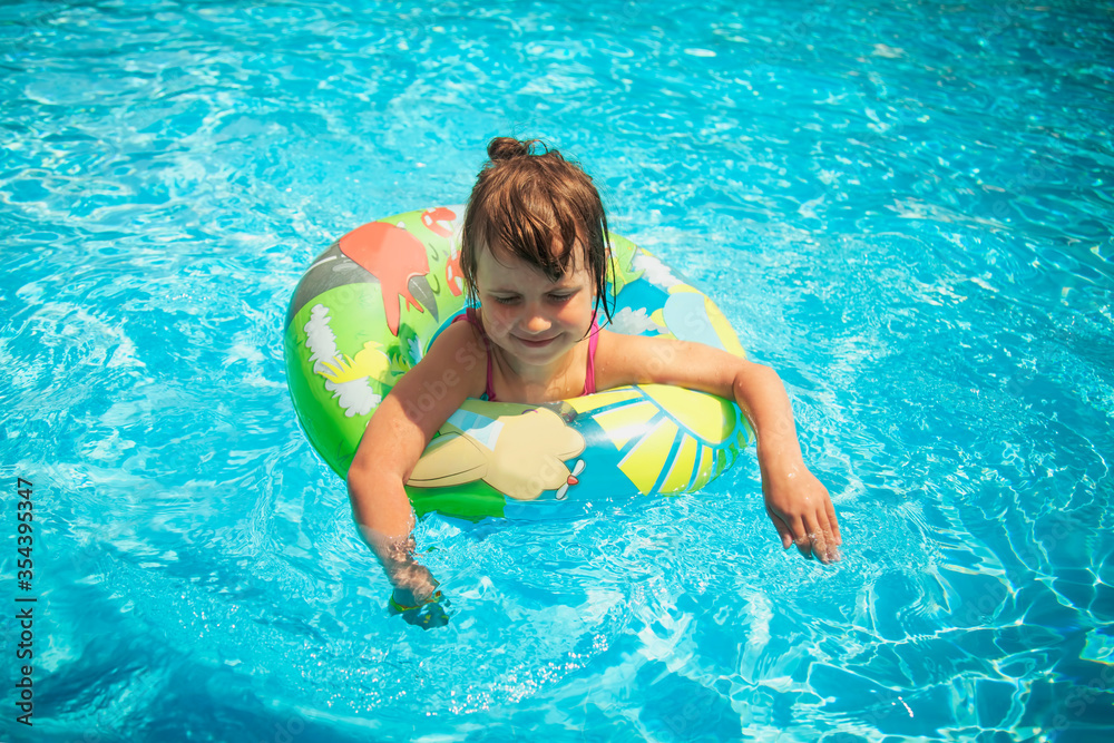 Summertime fun. Pretty little girl in the outdoor pool at the resort. Horizontal image.
