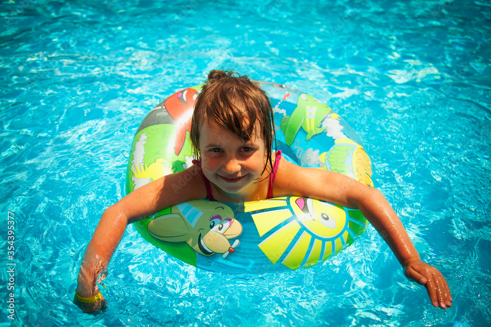 Pretty little girl in the outdoor pool at the resort. Summer holiday and happy carefree childhood concept.