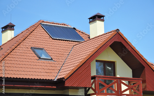 A modern house with metal tiled roof, skylight, solar panel, chimney, open balcony and window in the attic.