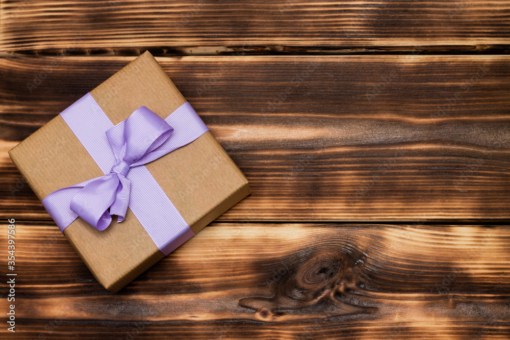 Gift in craft paper with a lilac ribbon on a rustic burnt wood background. Top view. Copy space. Gift in craft paper with a lilac ribbon on a rustic burnt wood background. Top view. Copy space.