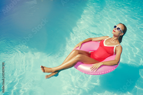 Enjoying suntan and vacation. Outdoor portrait of pretty young woman in red swimsuit with inflatable ring in swimming pool.