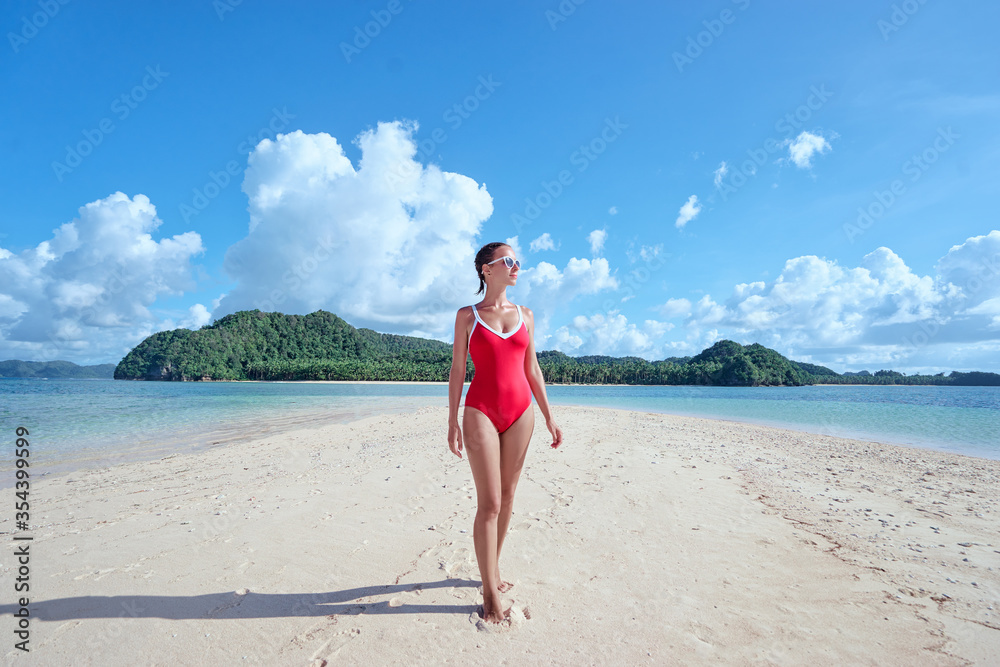 Vacation on the seashore. Young woman in red swimsuit walking on the beautiful tropical white sand beach. Vacation on the seashore. Young woman in red swimsuit walking on the beautiful tropical white sand beach.