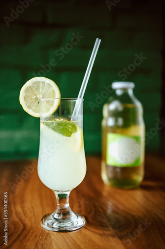 Fresh lemonade on the wooden table with glass bottle in the background