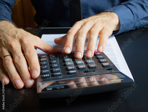 A young businessman calculates on the calculator the difference between the deficit and the surplus of the enterprise.