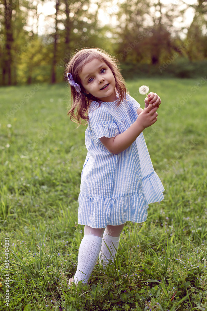 girl in a field with dandelions stands in a blue striped dress girl in a field with dandelions stands in a blue striped dress