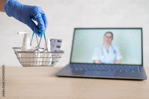 urchase of medicines using the computer application for home delivery. Pharmacist on laptop screen. A hand in a rubber glove puts on the table a basket with medicines and medical products photo