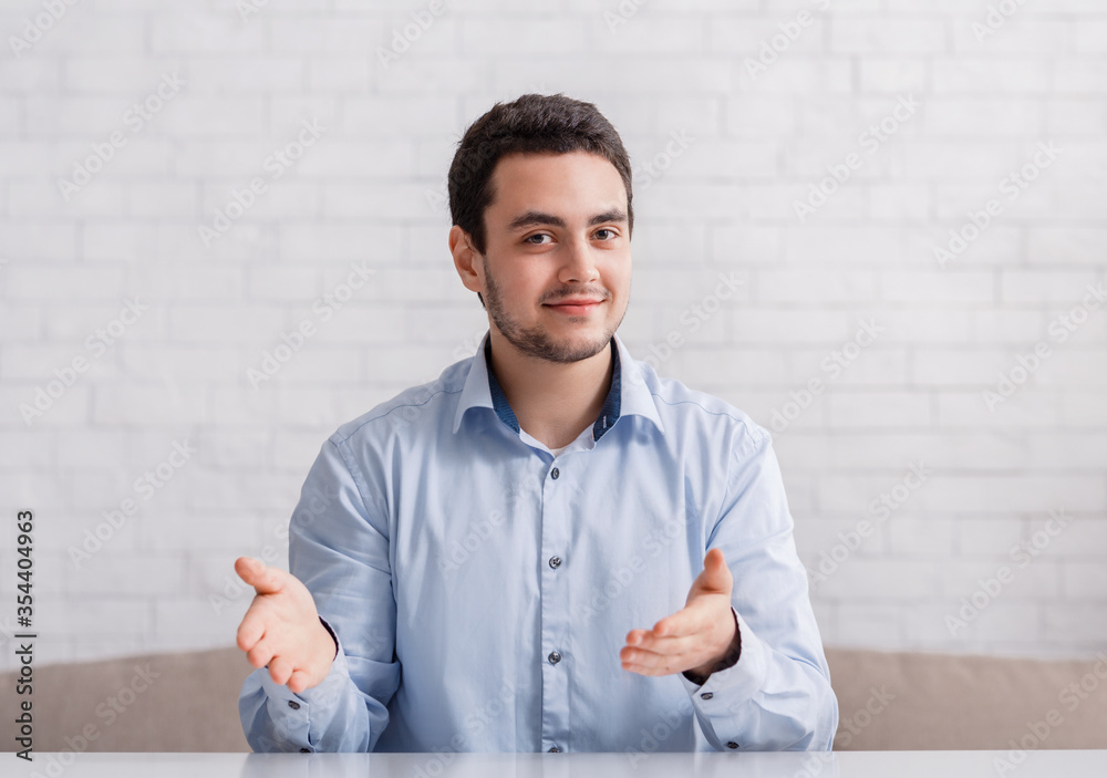 Friendly man point hands to empty space, sitting on couch in interior Friendly man point hands to empty space, sitting on couch in interior
