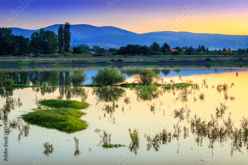 Golden hour sunset over calm, reflective lake with plants and small islands in the water and silky, glowing water, in Pirot, Serbia