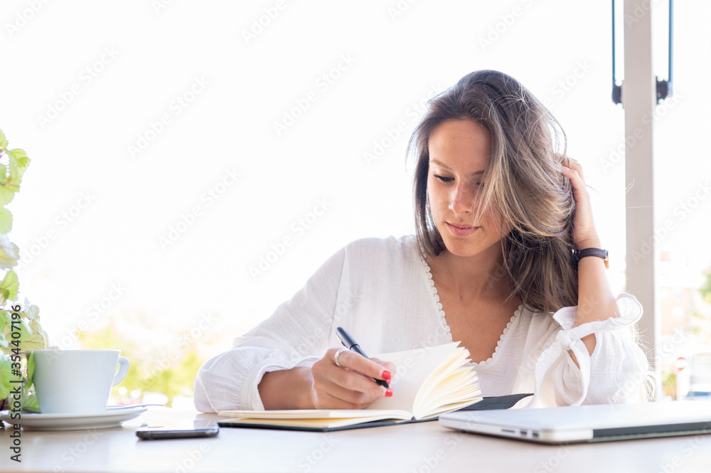 Young entrepreneur writes down in her notebook new ideas for her small business. On the table a cup of coffee, a smart phone and a laptop.Copy space