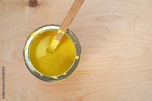 Old metal can with yellow paint on light brown wooden background. Mixing white paint, yellow color with stick. Painting boards, construction work and repairs in country. Space for text