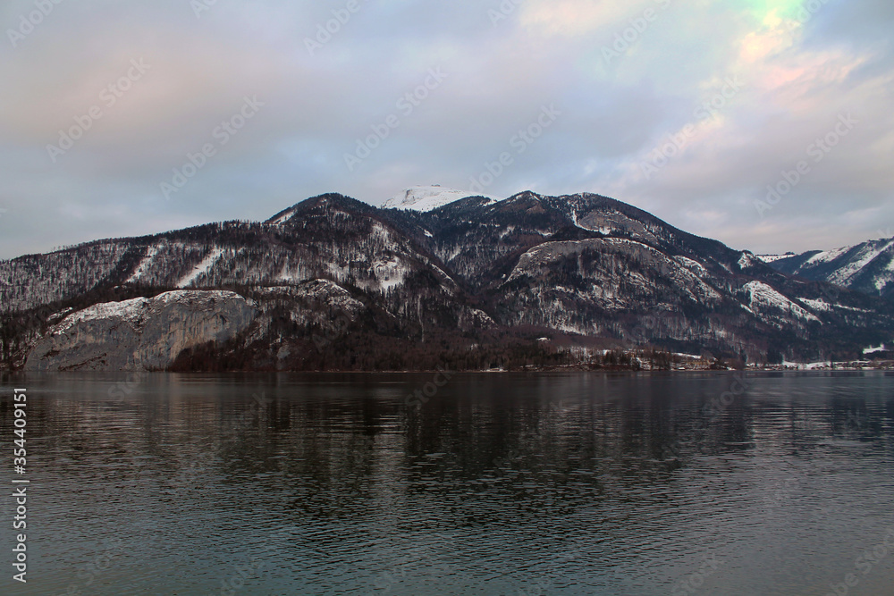Landscape of Wolfganfsee lake in Austria, surrounded by small mountains. The photo was taken in Wintertime during sunset time.