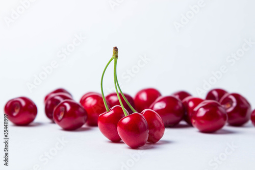 Three red cherries on one stalk. In the background a lot of red cherries. Red ripe sweet cherries on a white background