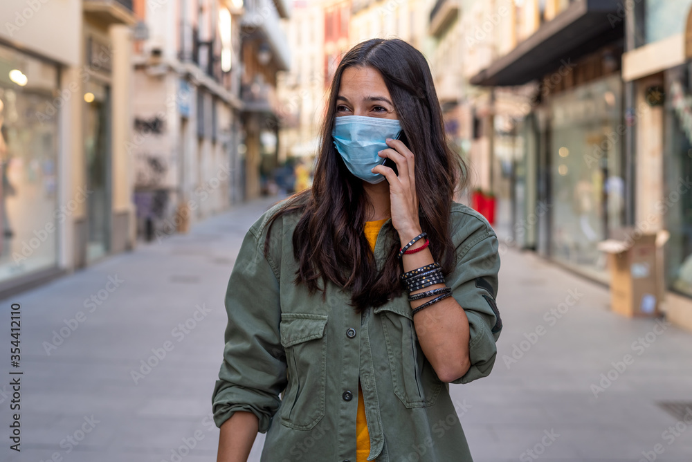 Fototapeta premium Woman wearing a protective mask on her face while using mobile phone in the street