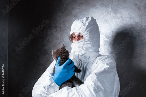 Veterinarian in a medical face mask and a viral protective suit. The vet holds a cat in his hands. The vet examines the cat.