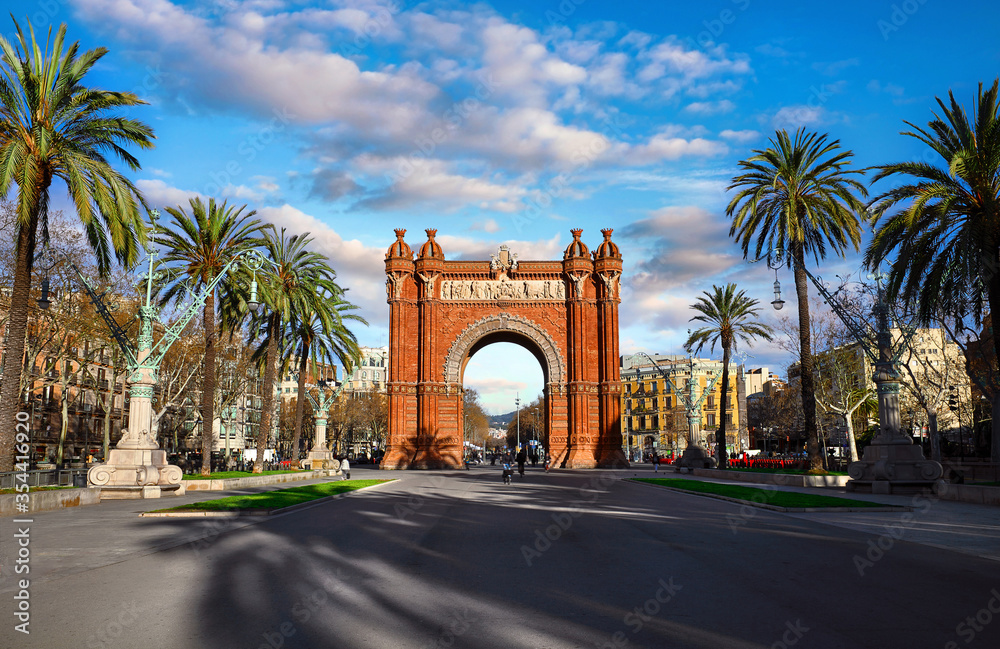 Triumphal Arch in Barcelona, Catalonia, Spain. Arc de Triomf at boulevard street. Alley with tropical palm trees. Early morning landscape with shadows and blue sky with clouds. Famous landmark. Triumphal Arch in Barcelona, Catalonia, Spain. Arc de Triomf at boulevard street. Alley with tropical palm trees. Early morning landscape with shadows and blue sky with clouds. Famous landmark.