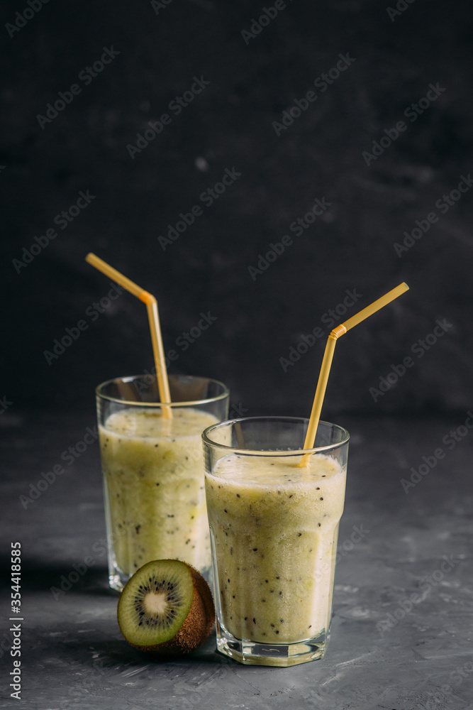 Fototapeta premium Kiwi and pear smoothies in glasses with a straw on a dark background side view
