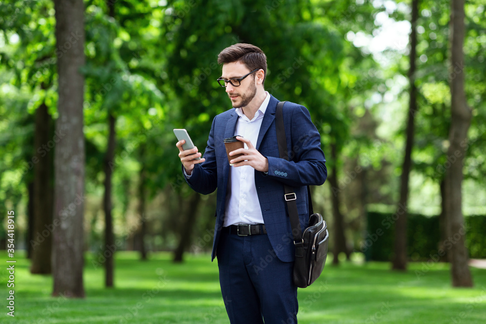 Confident businessman checking email on cell phone and drinking takeaway coffee in city park Confident businessman checking email on cell phone and drinking takeaway coffee in city park