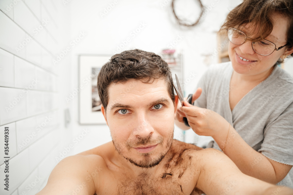 Haircut at home. A wife is cutting her husband with scissors in the bathroom. Haircut at home. A wife is cutting her husband with scissors in the bathroom.
