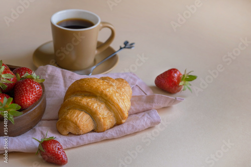 Croissant, cup of coffee and strawberries on a light background, selective focus. Breakfast concept. Copy space 