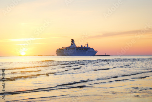 Large white cruise liner (passenger ship) sailing in the Riga bay of the Baltic sea at sunset. A view from the coast. Colorful cloudscape. Recreation, vacations, tourism theme. Latvia