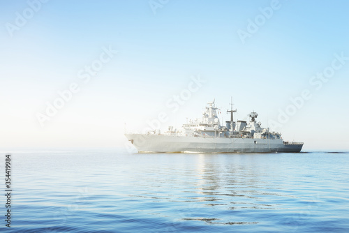 Large grey modern warship sailing in still water. Clear blue sky. Baltic sea, Germany. Global communications, international security theme