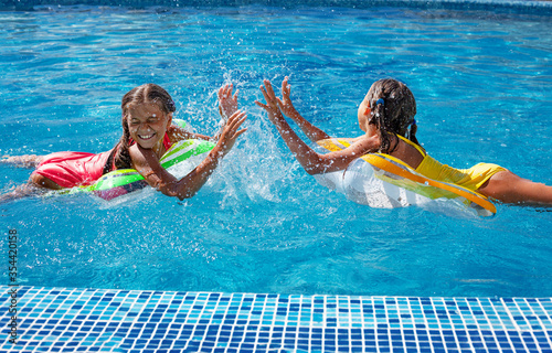 Canvas-taulu Two tween girls playing, splashing, laughing and have fun in the blue water of swimming pool with inflatanle rings