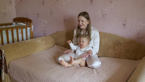 Beautiful attractive mother with a cute baby sits at home on the couch and has fun watching TV.