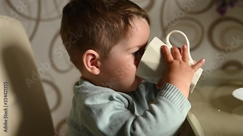 Little child drinks water from a mug on his own. Independent baby